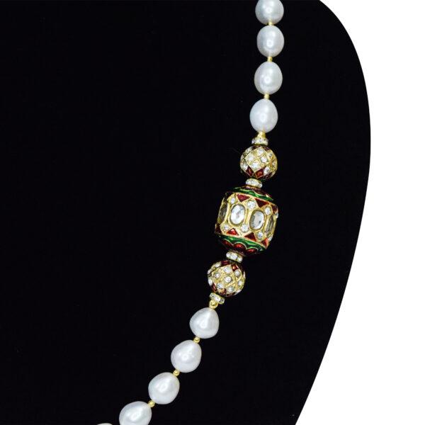 Single-layer oval white pearl necklace interspaced with golden colour beads attached to meenakari dholak beads as a brooch on the side - close up